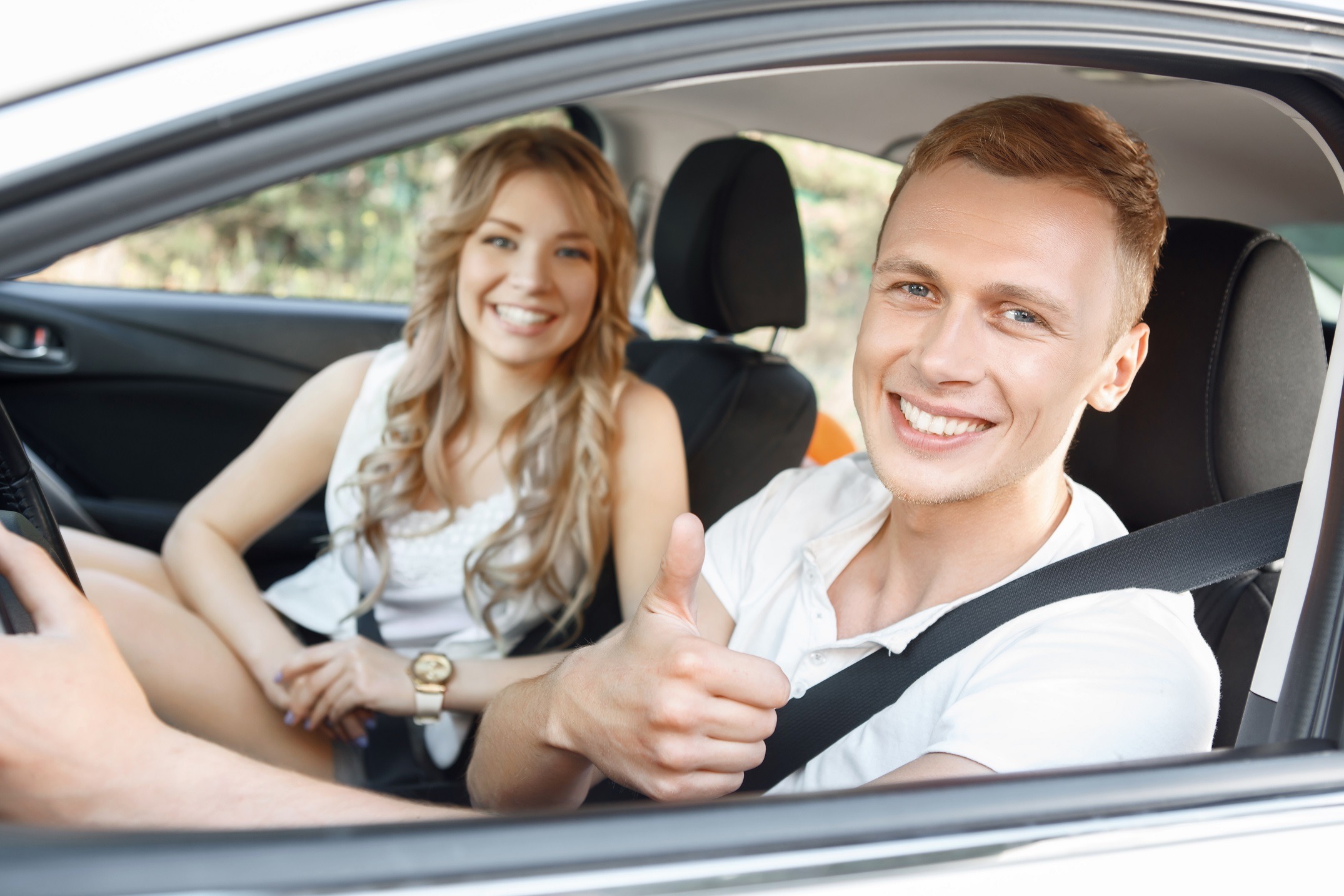 Young smiling couple in the car and showing thumbs up