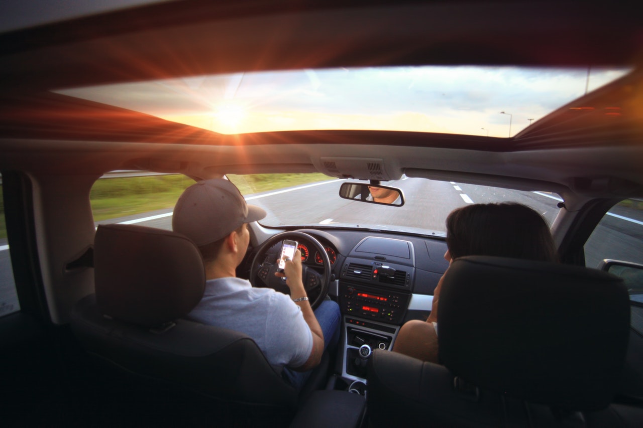 man typing text message while driving a car