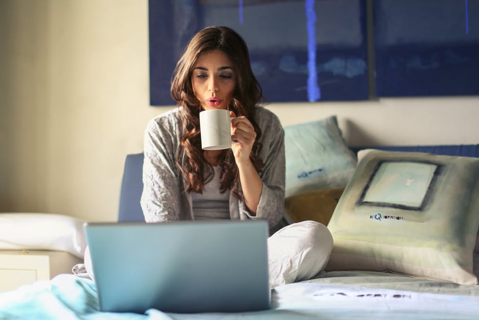 woman sits on bed uses grey laptop