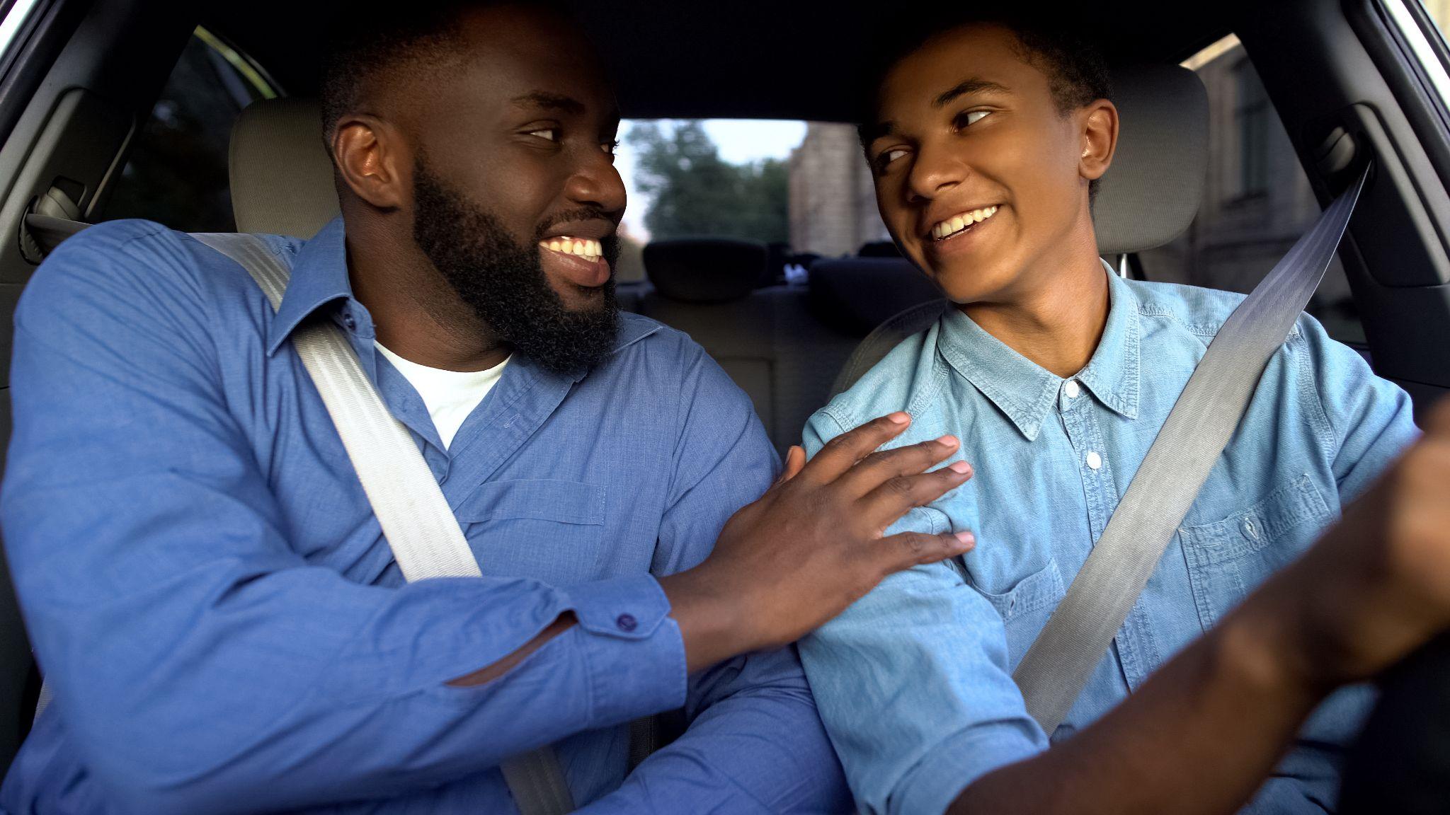 Smiling father praising son learning to drive auto