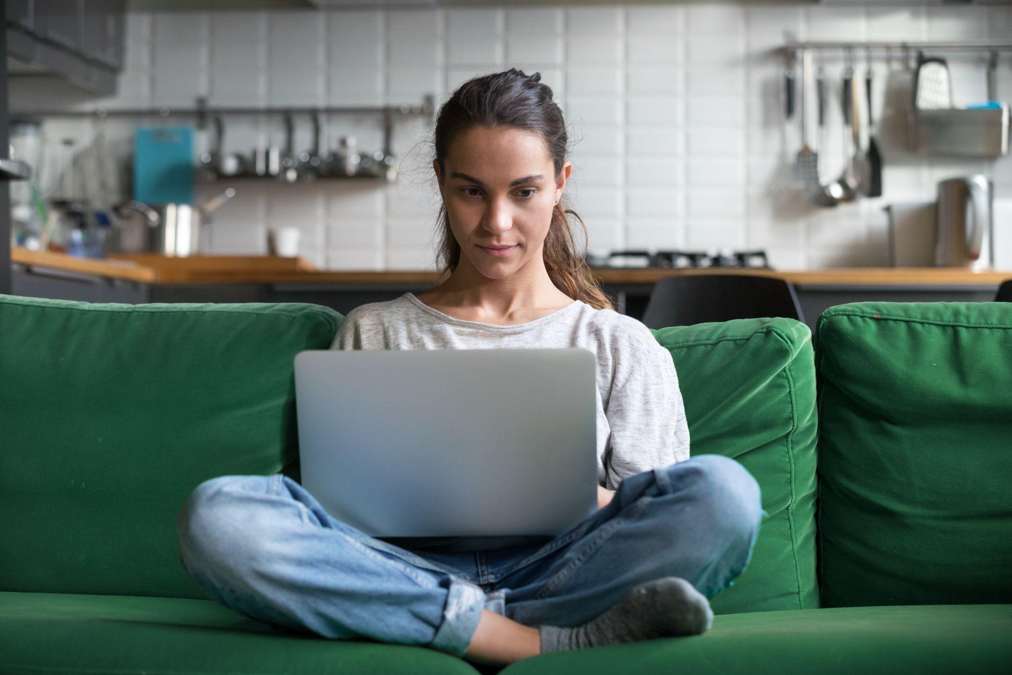 Serious woman using laptop checking email news online sitting on sofa