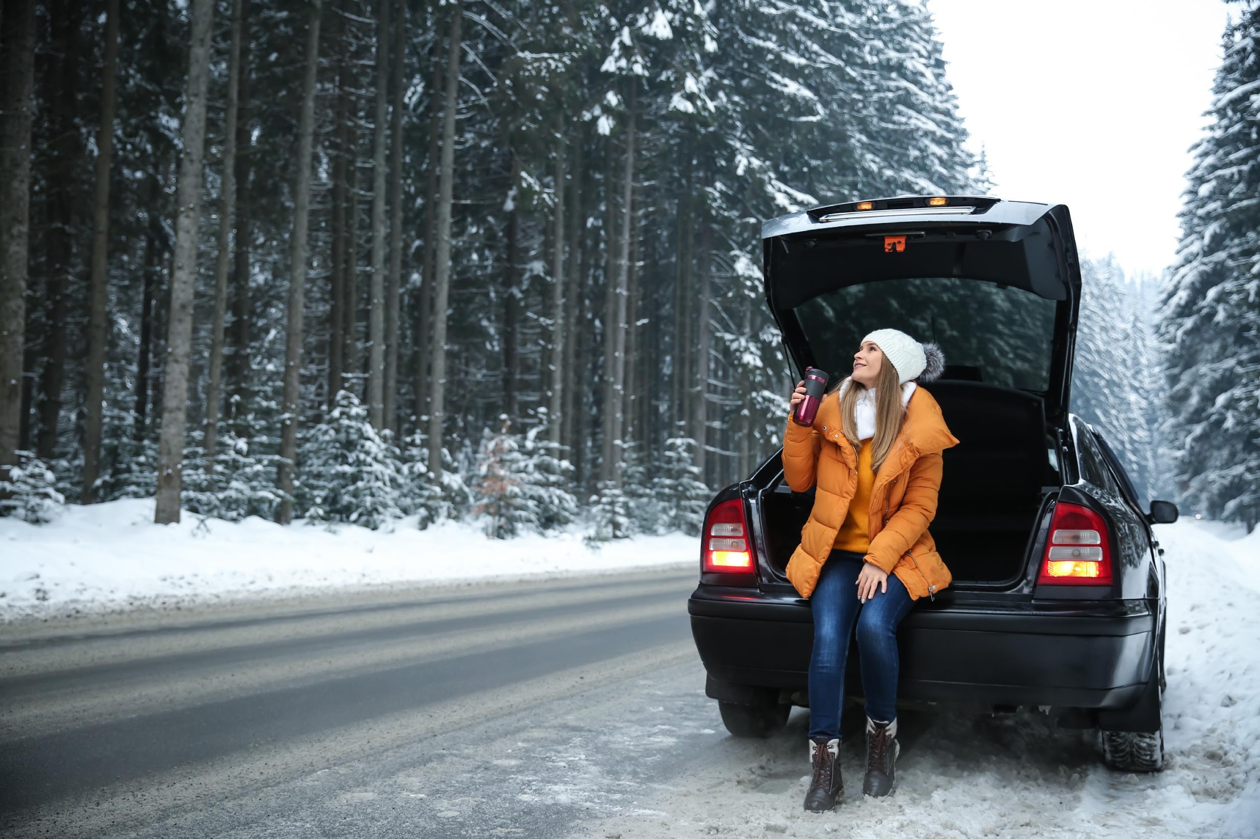 Female tourist drinking coffee near car in snowy countryside