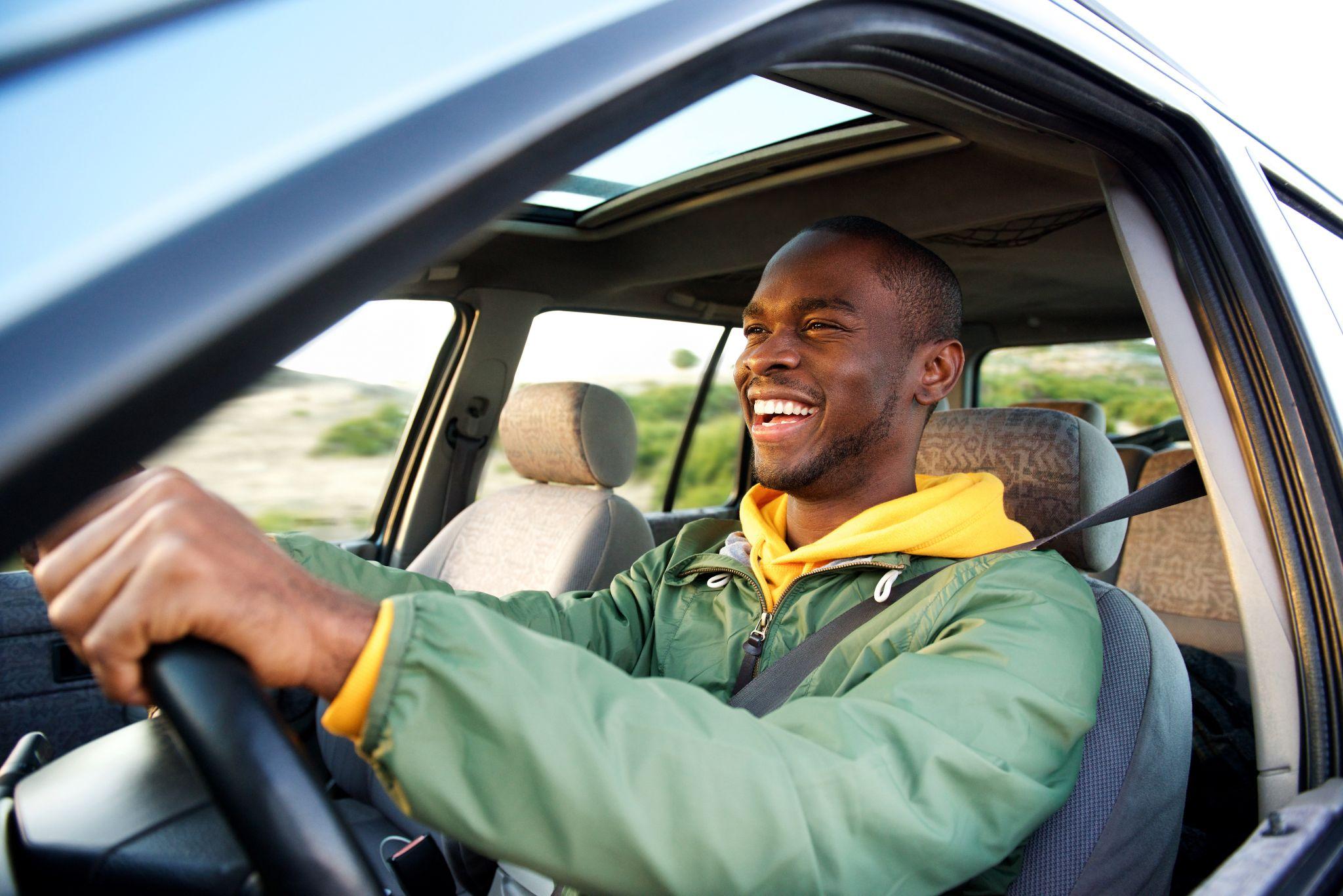 Side of happy african american man driving car