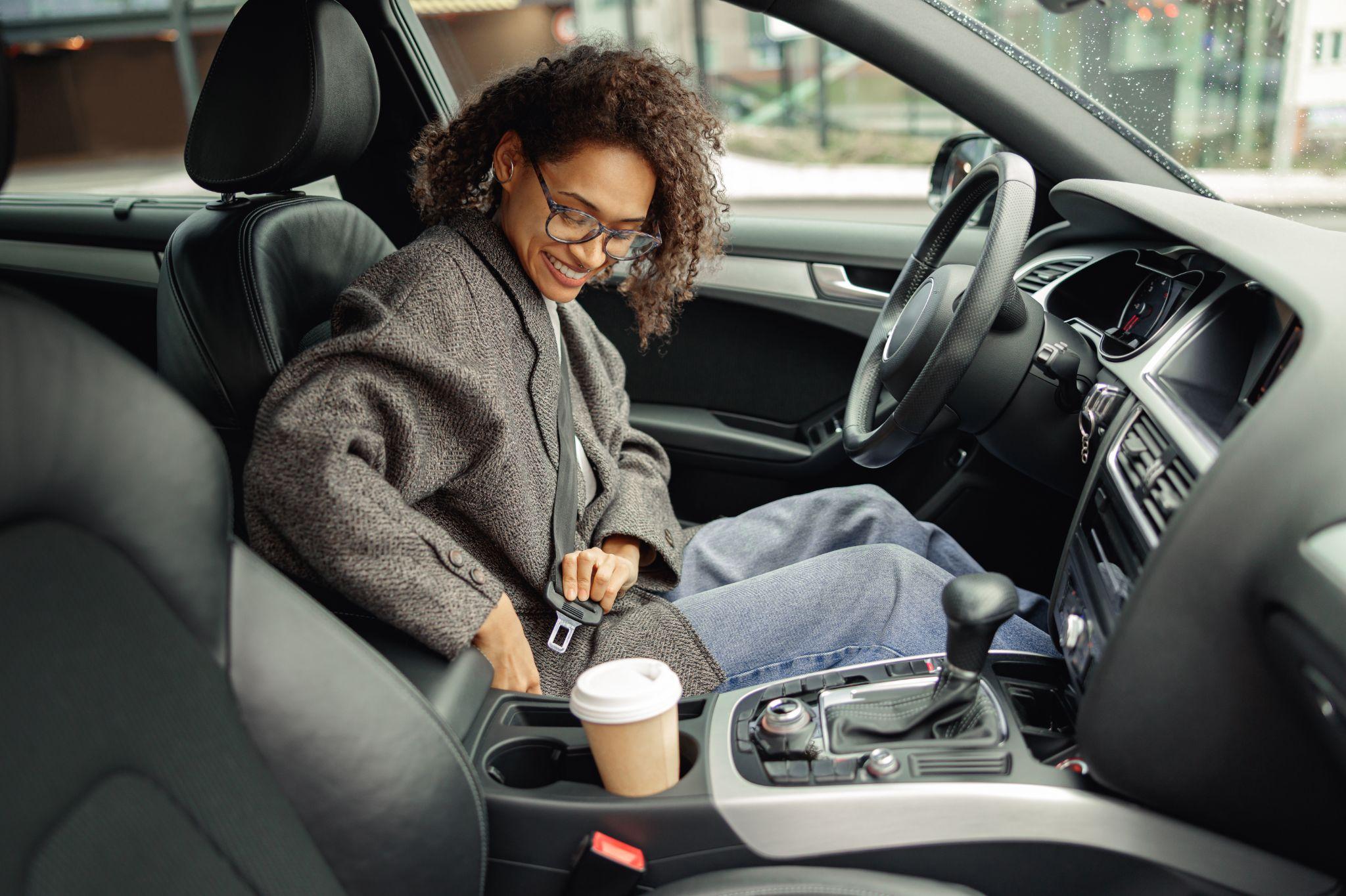 Smiling woman driver in eyeglasses fastens her seat belt before starting car. Driving safety concept