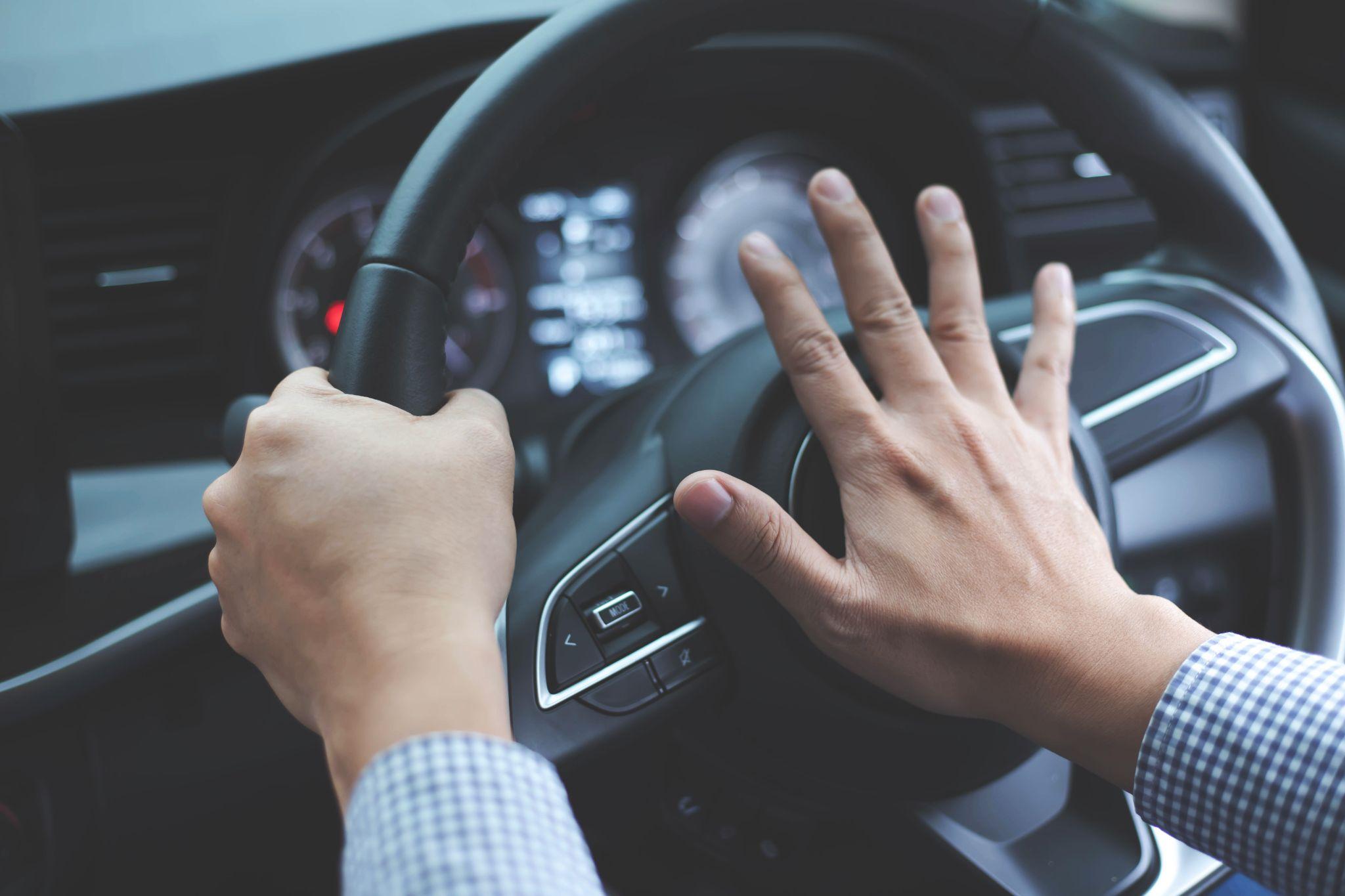 Close up image of inside the car of the hand pressing the horn on the steering wheel.