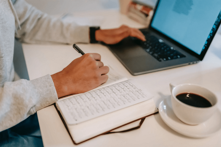 Young man writing in notebook near laptop