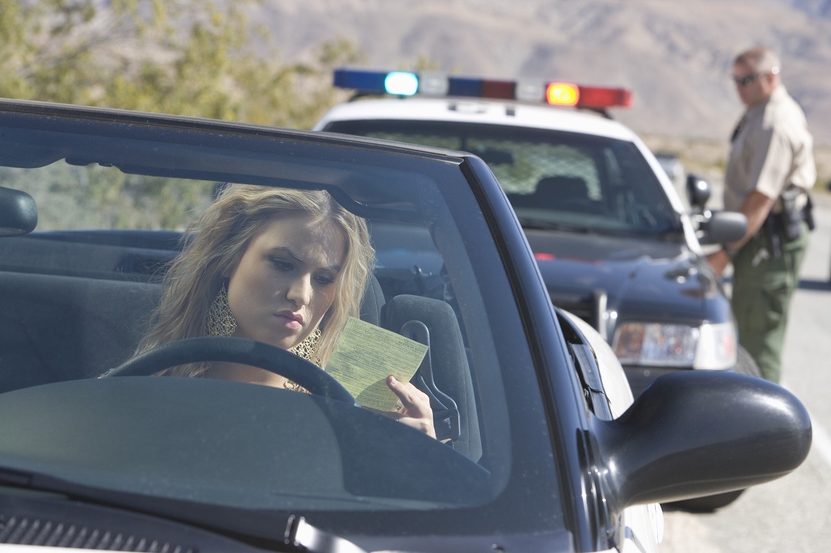 Young woman in car reading ticket with traffic cop in the background