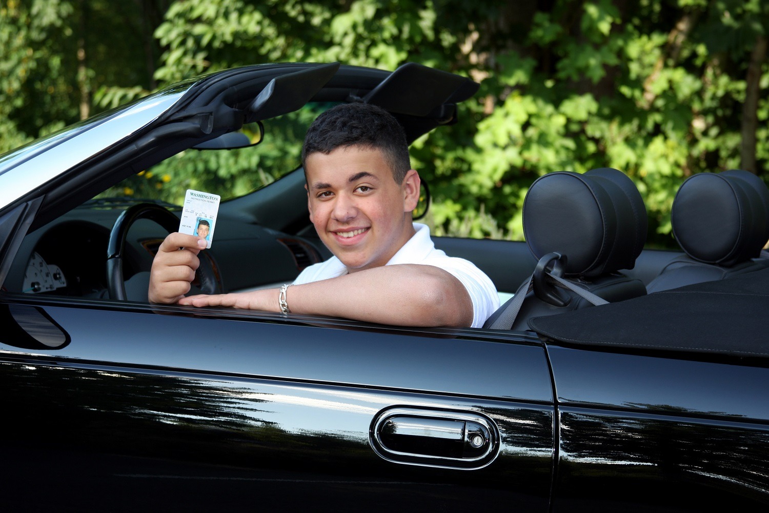 a teenage boy in a convertible holding his drivers permit