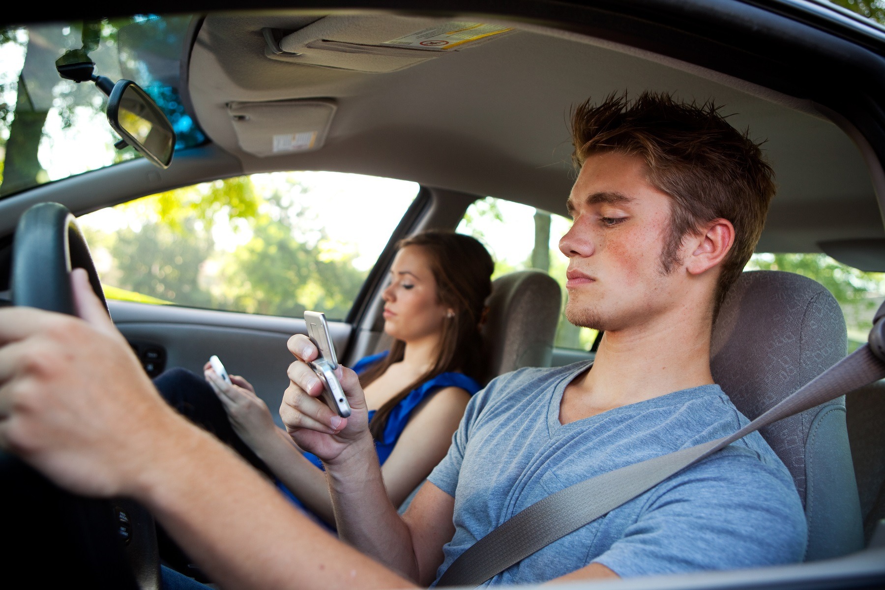 two teens driving car with texting and looking at cel phones while in motion