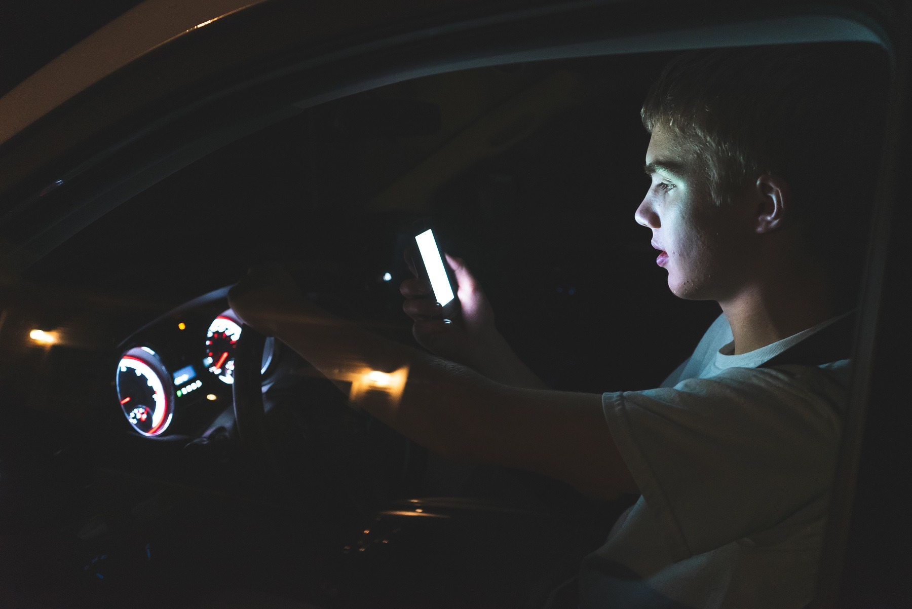 Distracted teenager driving a car with his cell phone in his hand