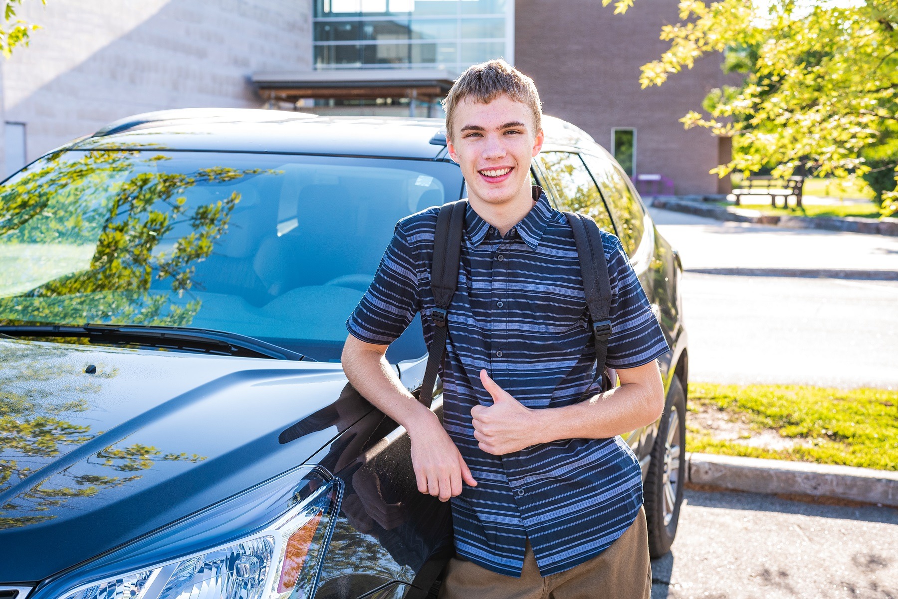 Happy male teenager leaning against his car