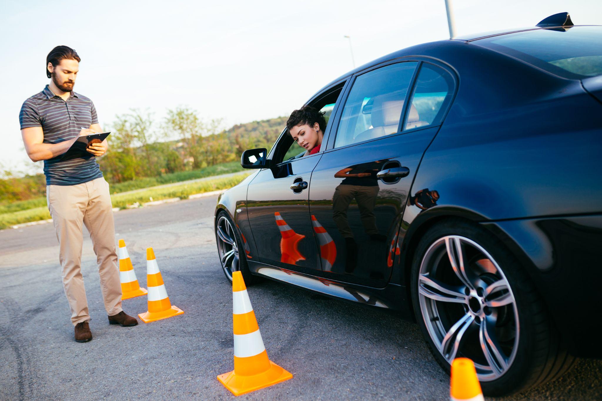 Beautiful young woman with instructor learning how to drive and park car between cones.