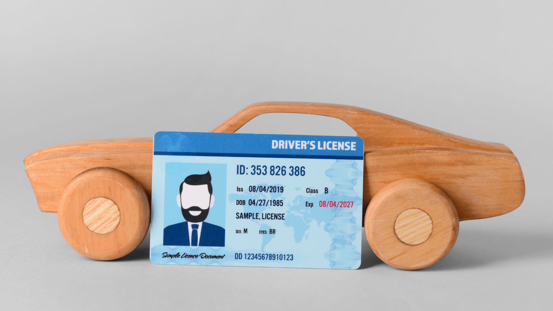 Wooden car and driving license on grey background