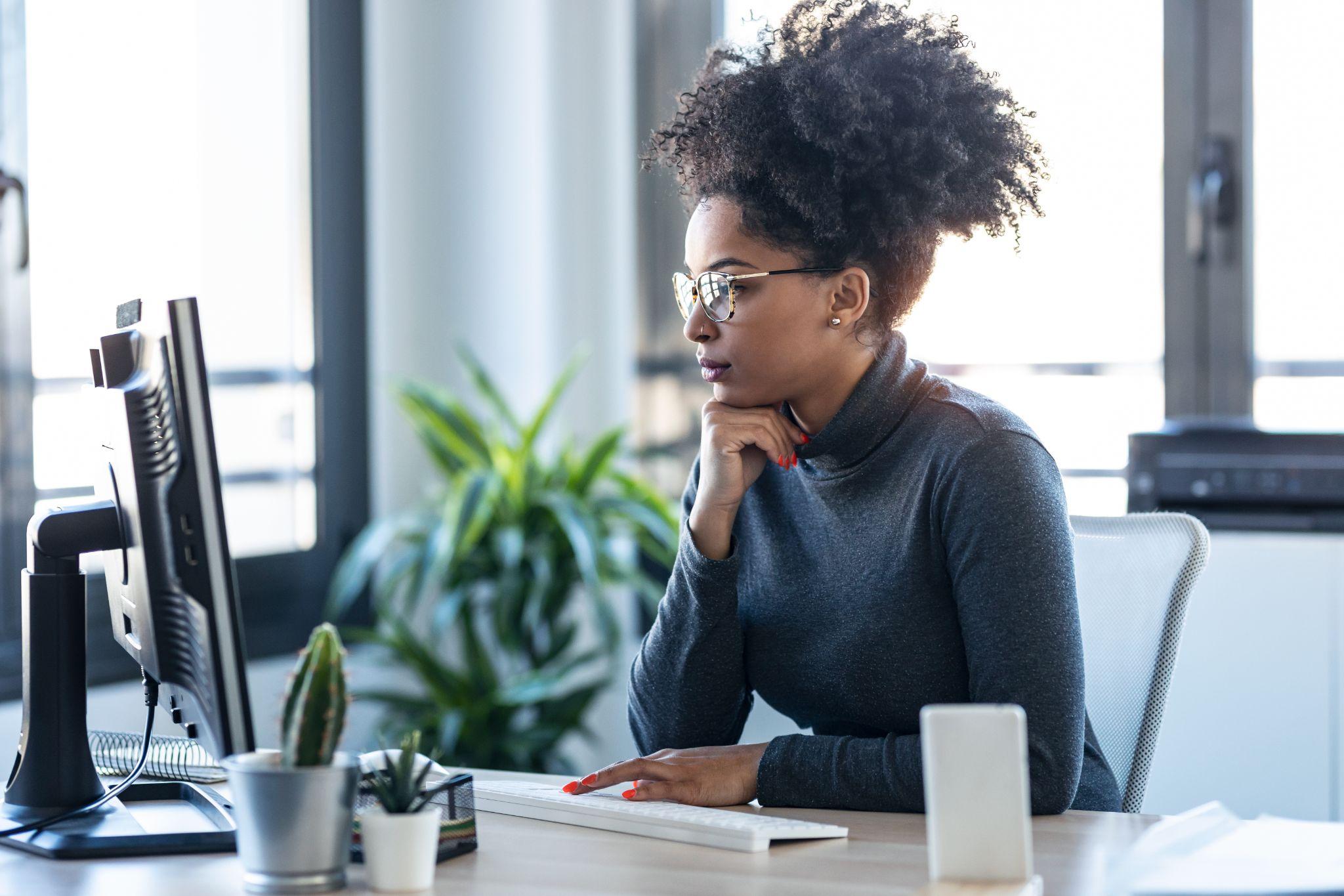 Beautiful young afro business woman working while making video call with computer sitting in the office.