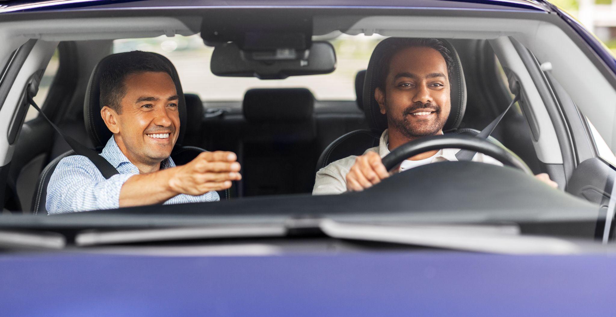 happy smiling car driving school instructor teaching young man to drive