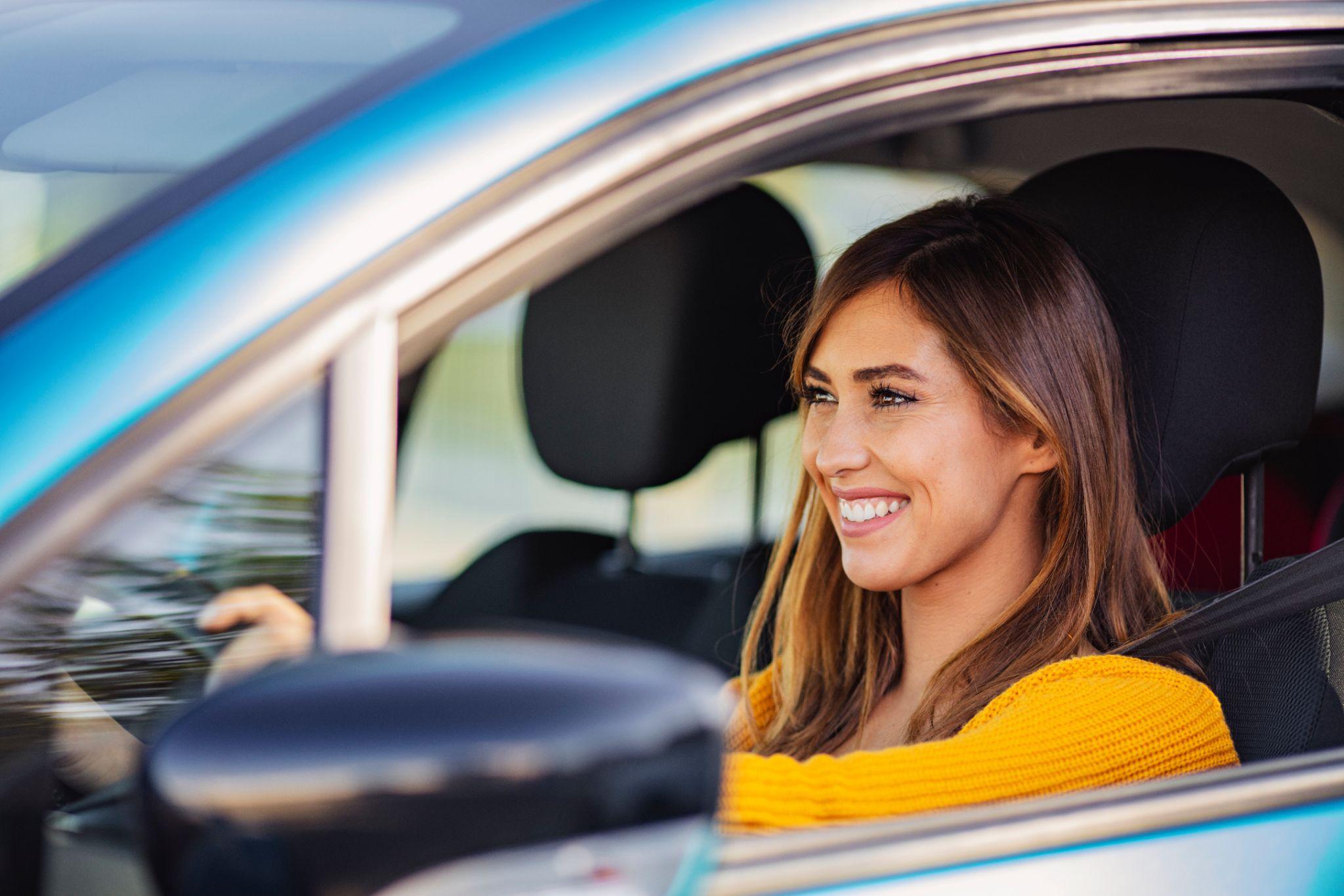 Young smiling woman driving a car drives around the city.